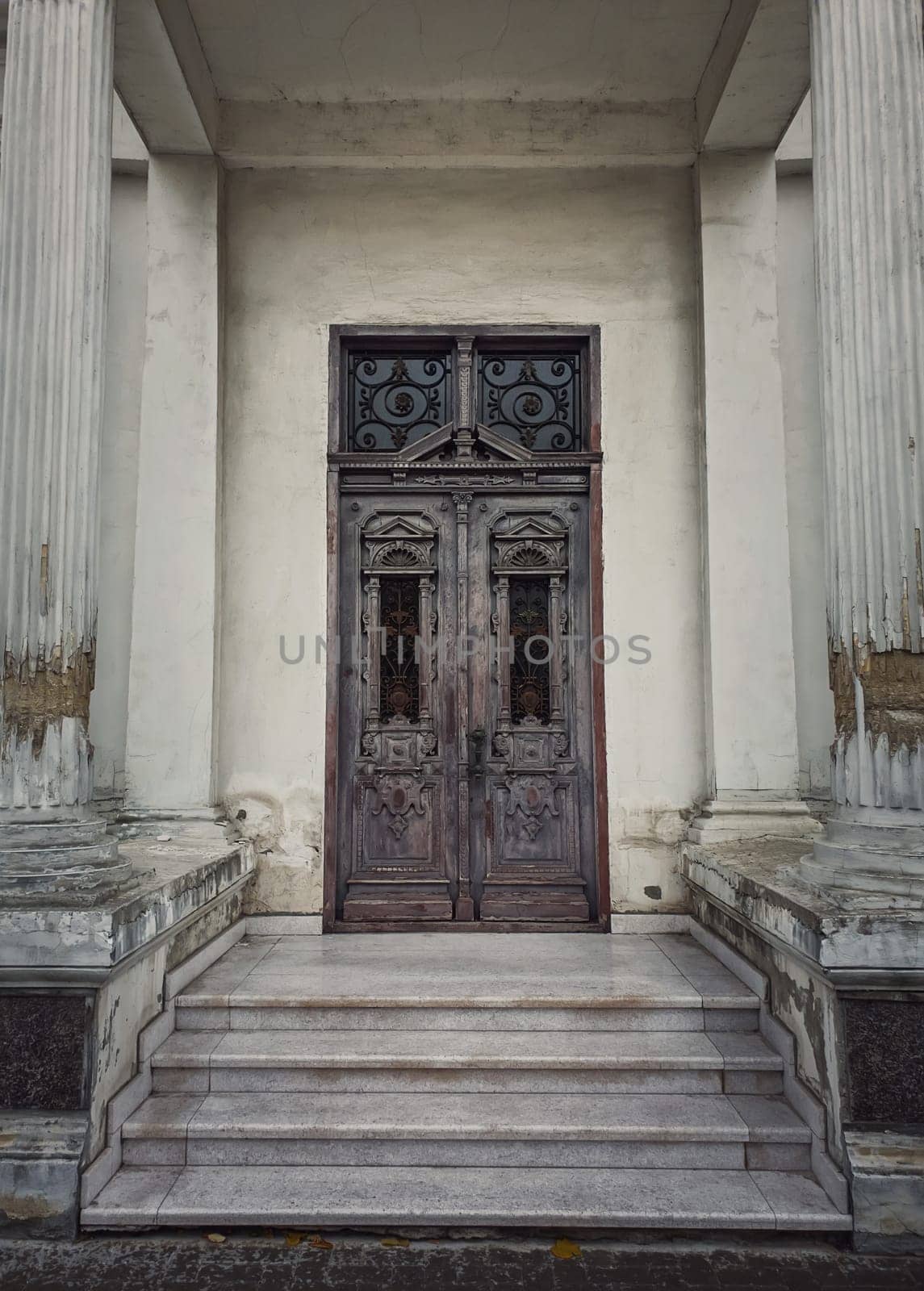 Vintage door and ornate facade details of an old historical building. Outdoors architecture elements, white columns on the doorsteps. Rustic wooden gate. The main entrance doorway