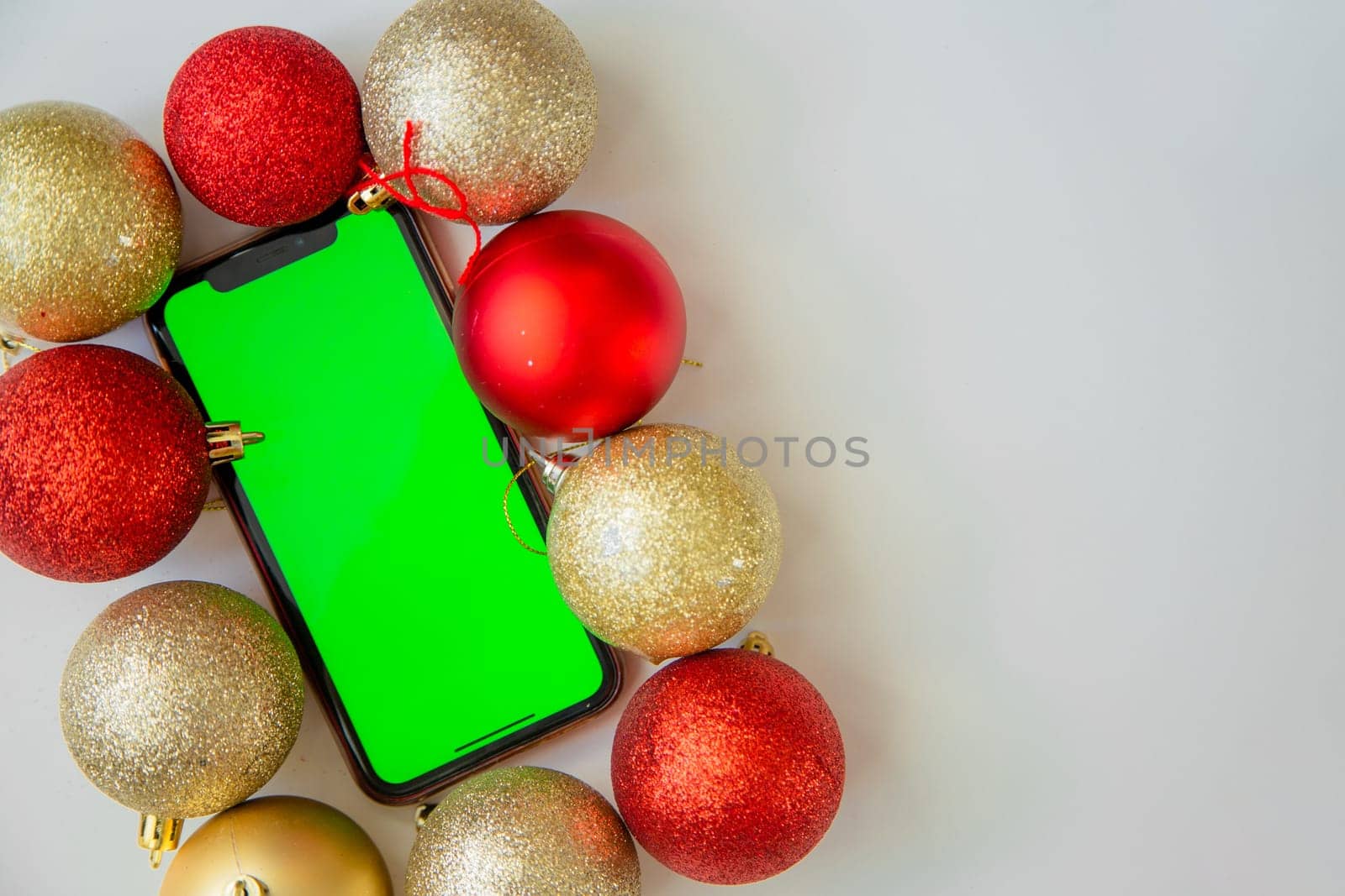 A phone with a green screen lies among the golden and red Christmas balls. High quality photo