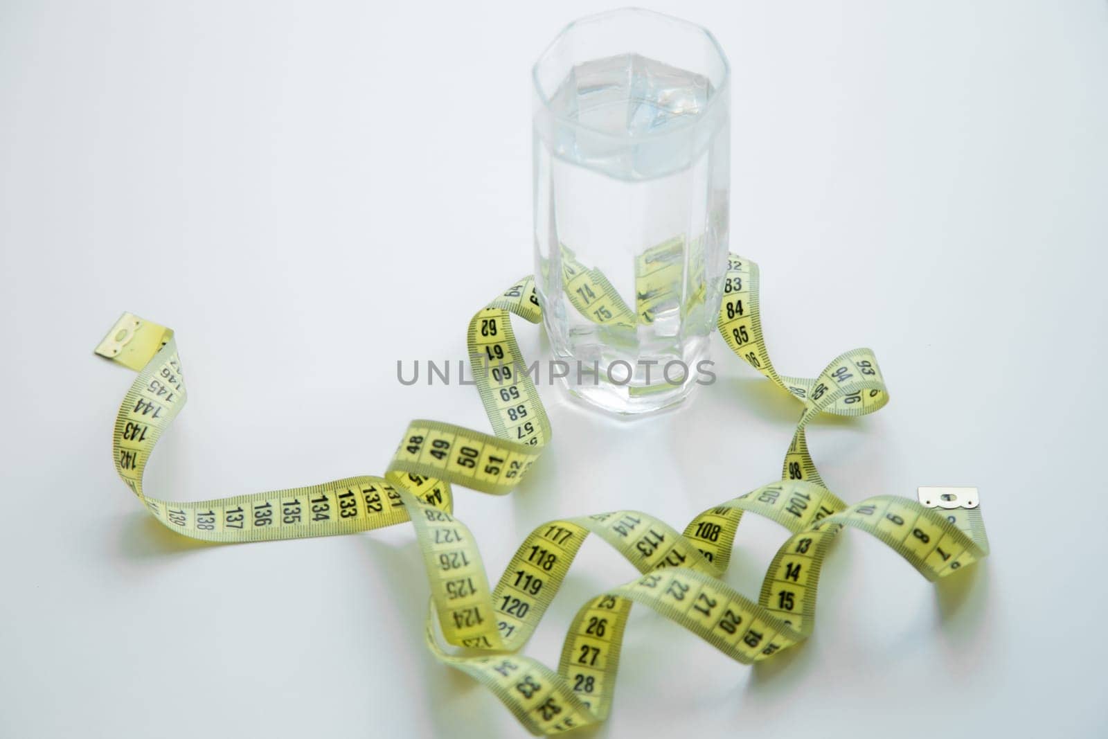A green apple and a glass of water stand on a white background, they are entwined with a measuring tape. High quality photo