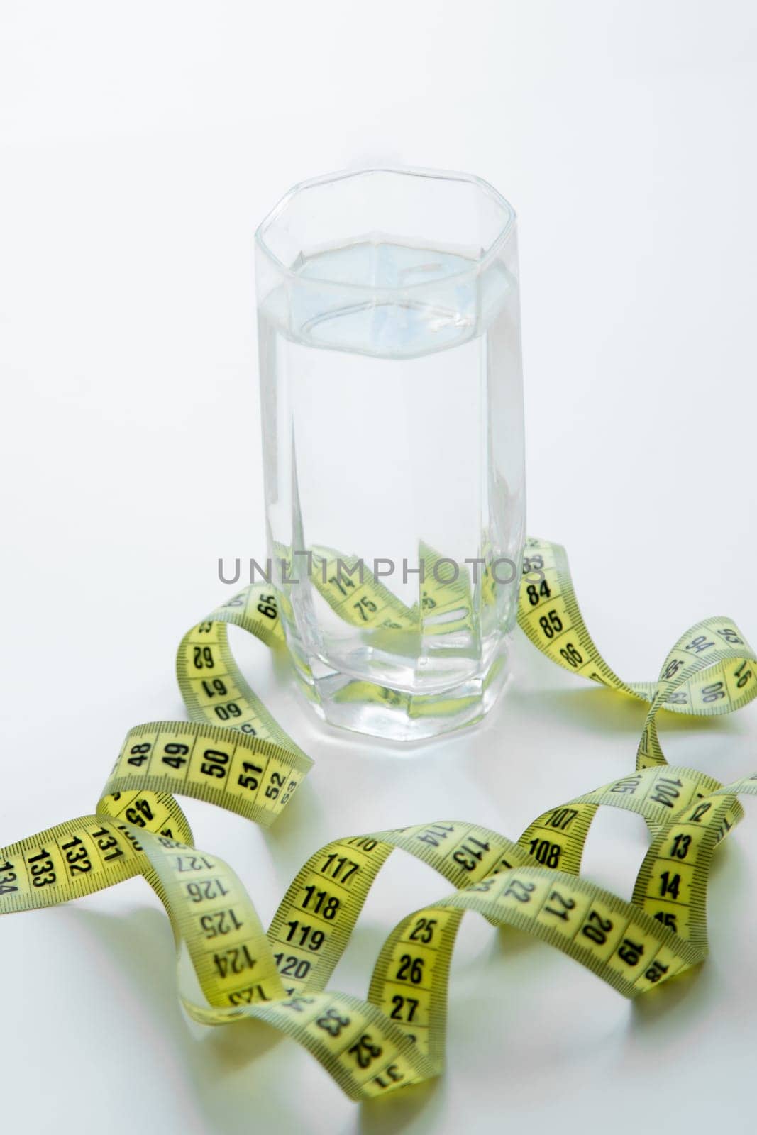 A glass of water is wrapped with a measuring tape on a white background. . High quality photo