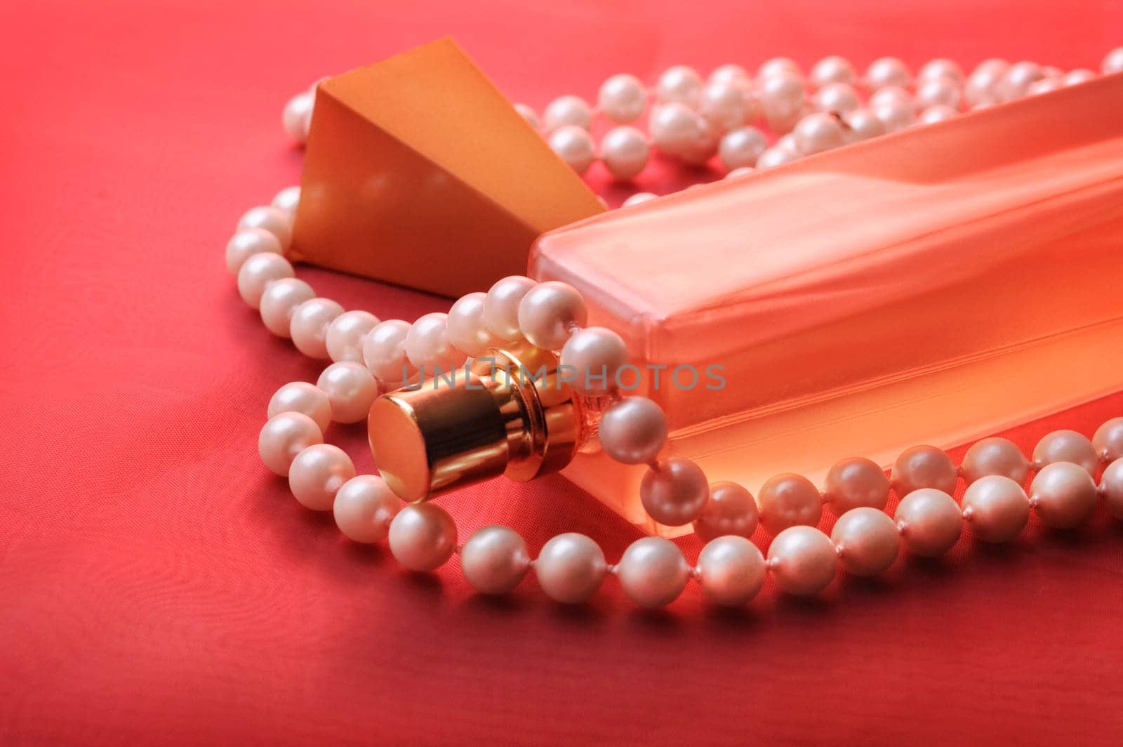 Bottle of perfume and pearls on purple silk