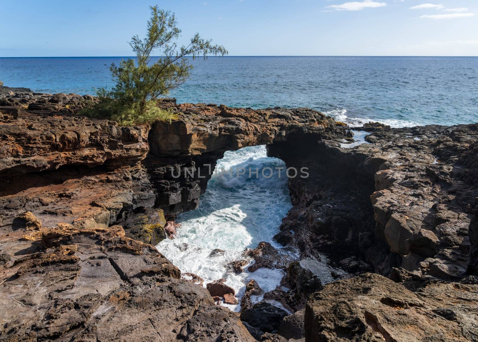 A natural lava arch provides a stunning contrast to the bright blue ocean at Poipu, Kauai, creating a beautiful coastal scene.