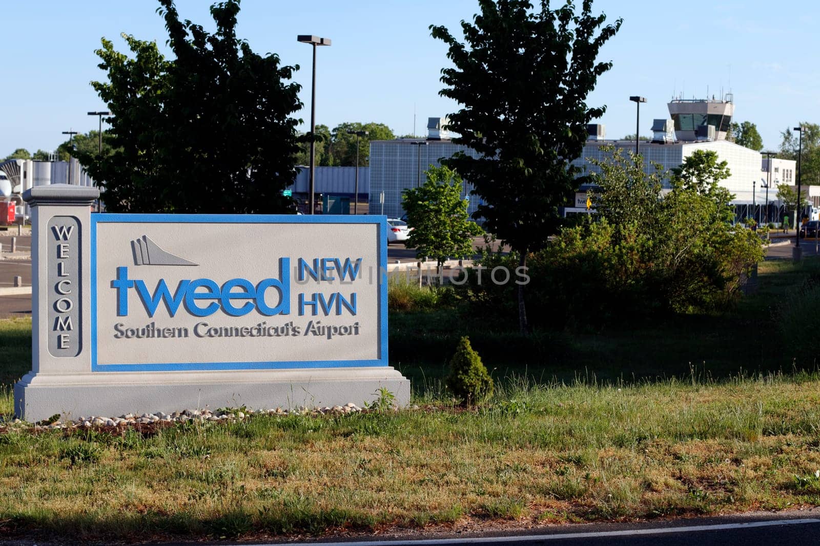 New Haven, CT, USA - May 27, 2021: Entrance sign to Tweed New Haven airport code, HVN, on a sunny evening with airport in back. Tweed New Haven airport entry sign with airport and a plane in background.