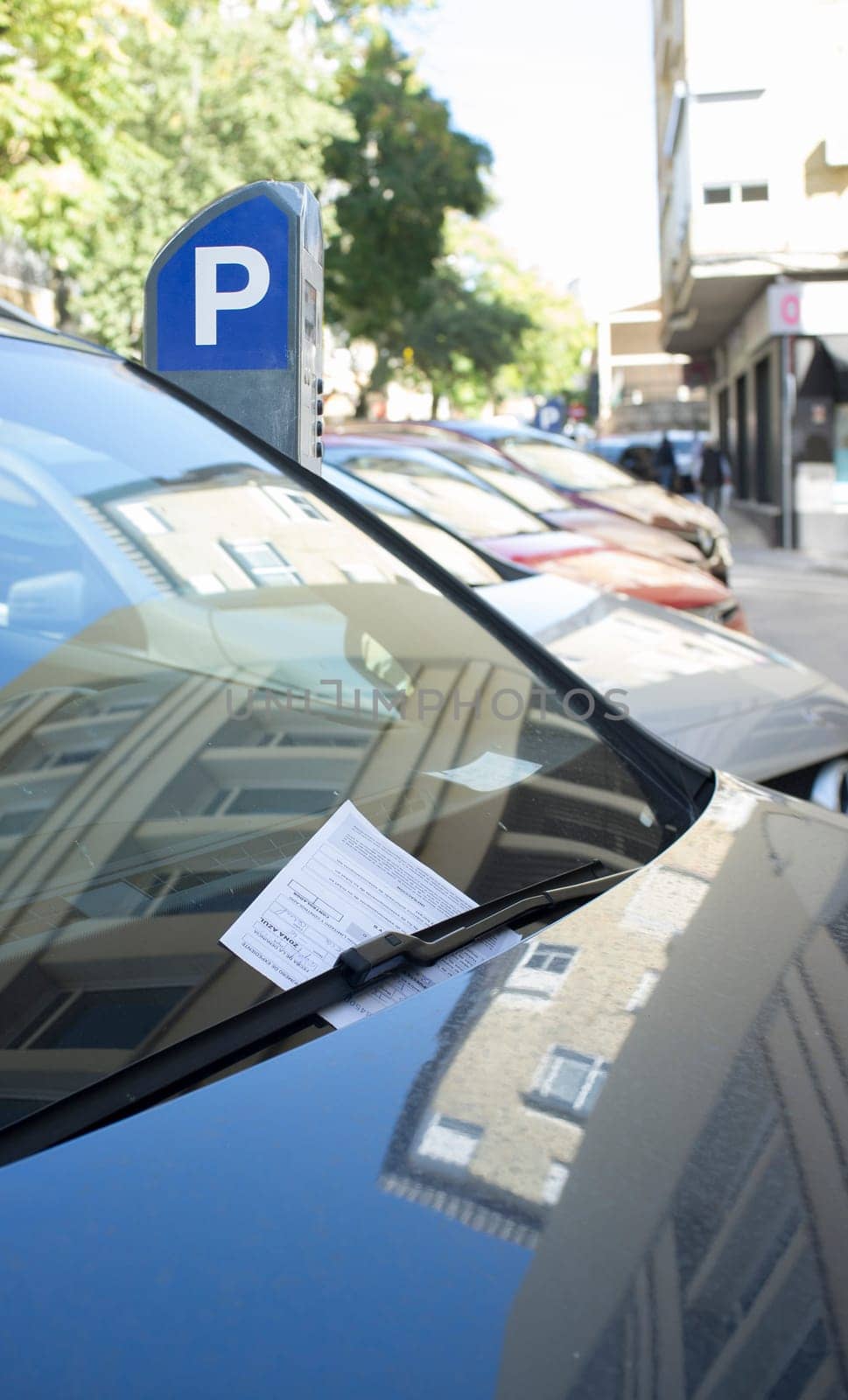 Vehicle fined for having parked in the blue zone. Ticket under the windshield wiper with parking meter at the bottom