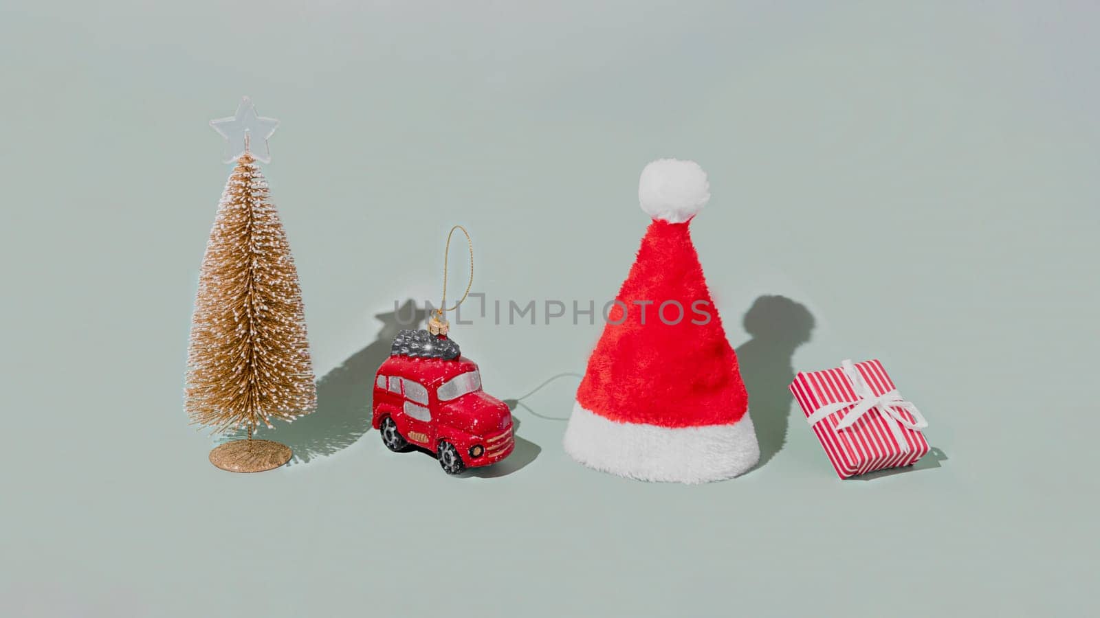 Gray background with Christmas or New Year symbol attribute objects and symbolic items concept. Pink gift box present with ribbon, small red taxi car toy, fir tree and red festive santa hap or cap