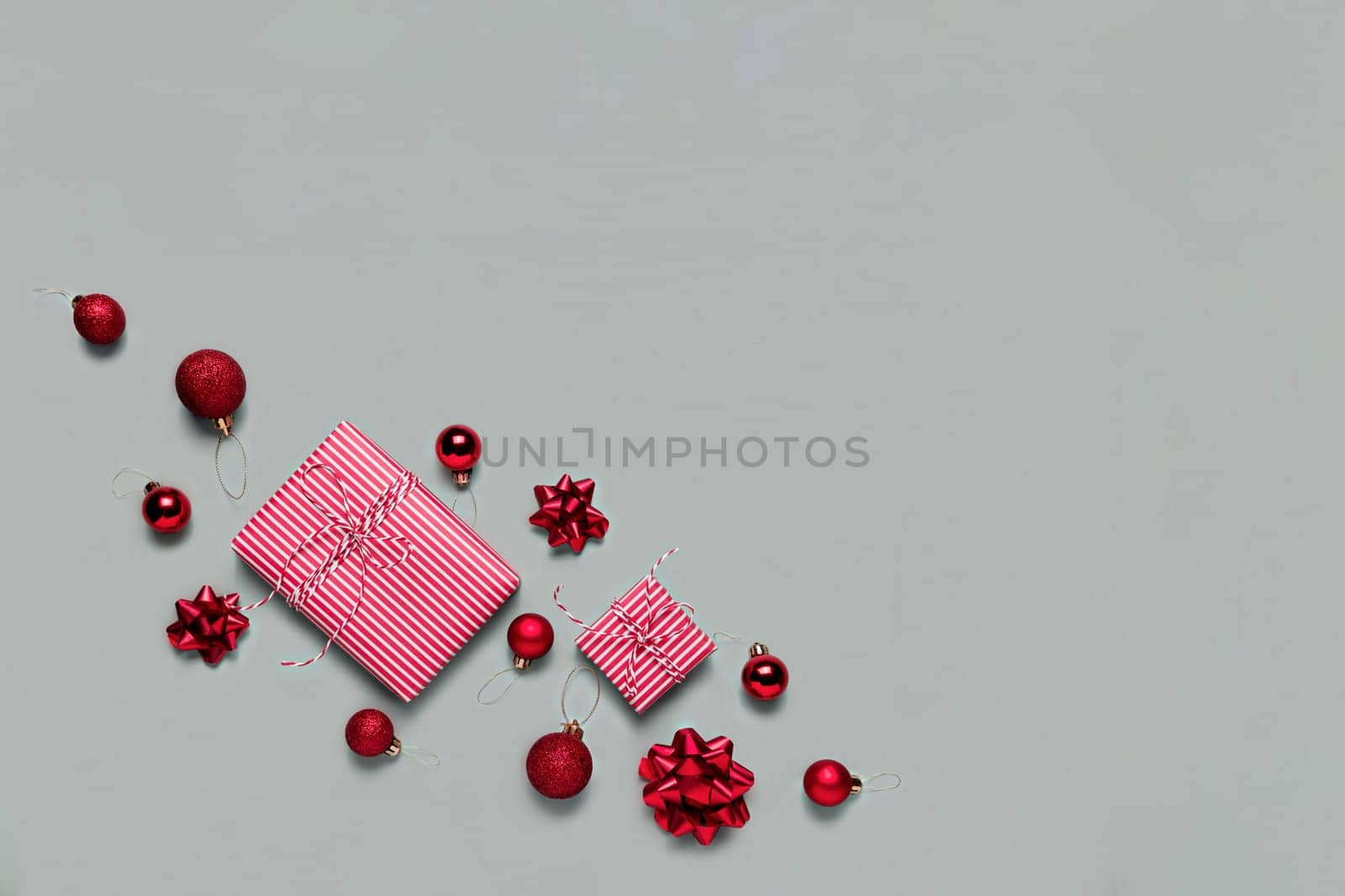 Gray background with two pink Christmas gift box presents, small red Christmas balls or sphere toys, ribbon bows for fir tree. Concept for festive sales, promotions, greeting card or invitation photo