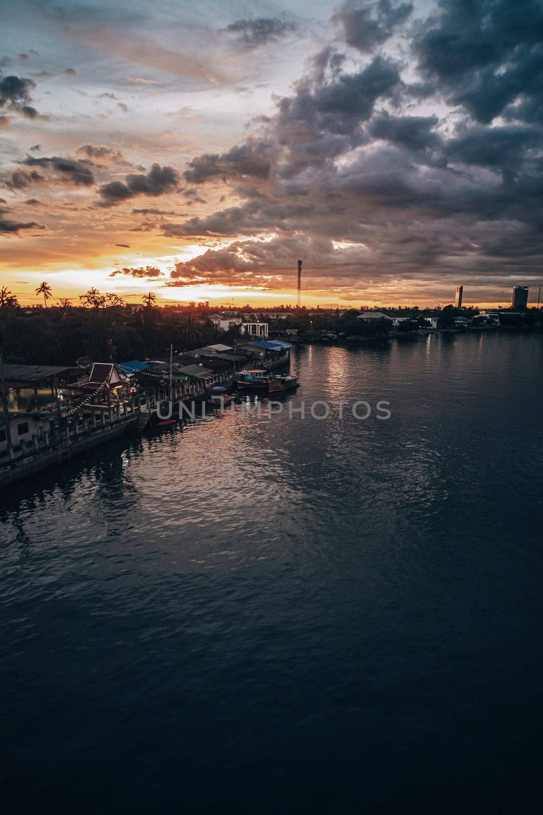 Panorama Cityscape at sunset with large river at foreground and storm clouds at background in Thailand.