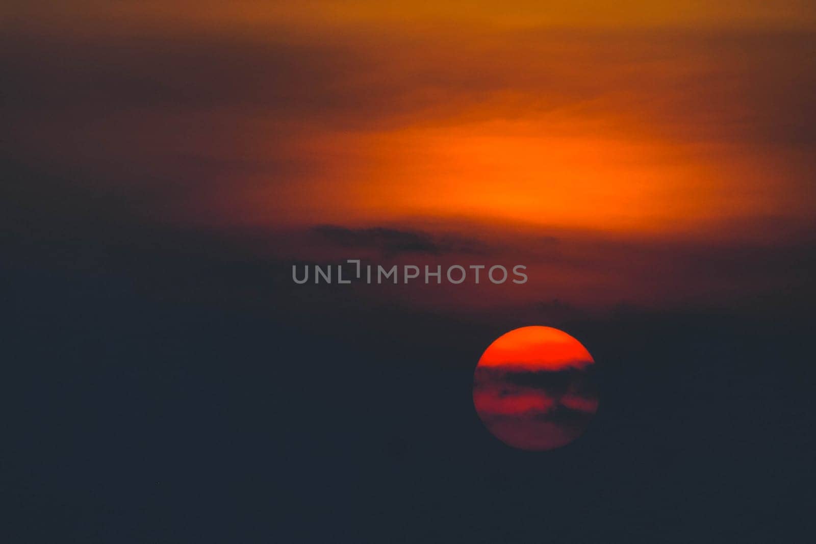 Beautiful sunset. Dramatic Fiery Sun Surrounded by Clouds During Sunset.  Vibrant orange red clouds are back lit by the sun.