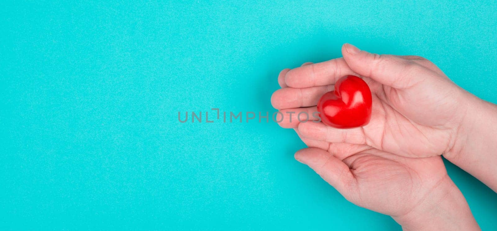 Woman is holding a red heart in her hand, blue colored background, copy space
