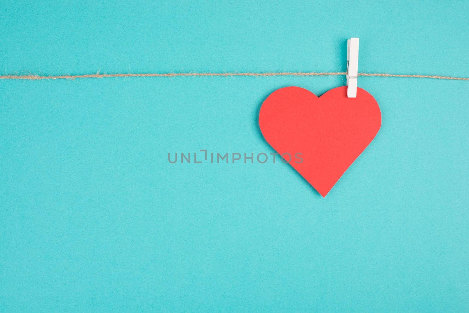 A heart hanging on a clothing line, blue colored background, empty copy space, symbol of love, valintine greeting card