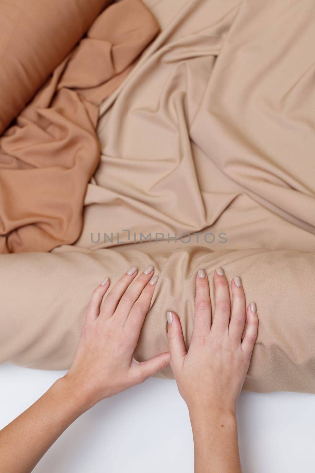 Female tailor hands rolls up beige fabric roll. Top view, flat lay