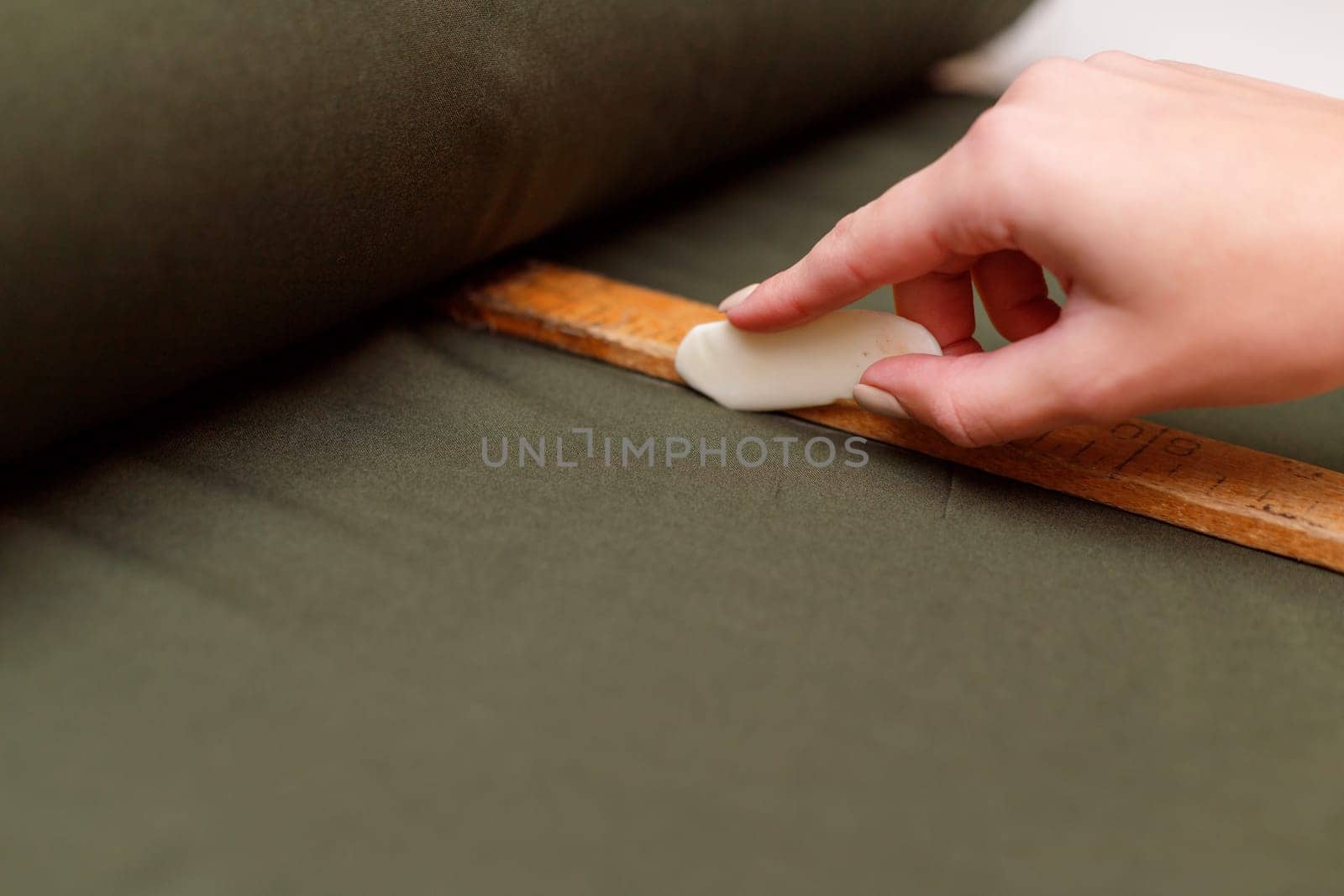 tailor marks up textile using soap and wooden ruler on pattern cutting.