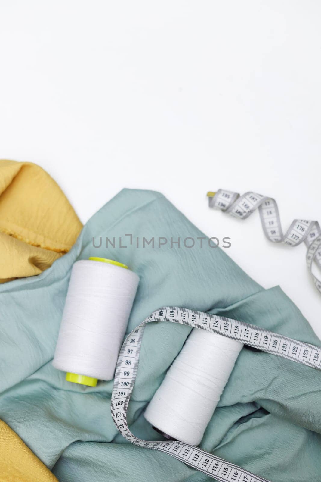 Various fabrics, measuring tape and thread isolated on white. Flat lay
