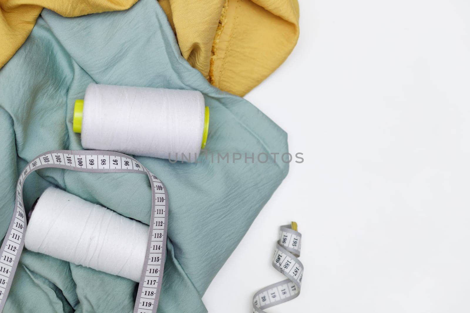 Various fabrics, measuring tape and thread isolated on white. Flat lay