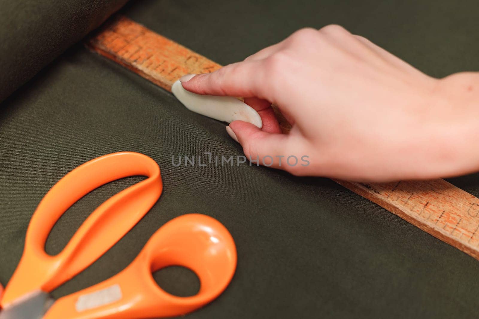 tailor marks up textile using soap and wooden ruler on pattern cutting.
