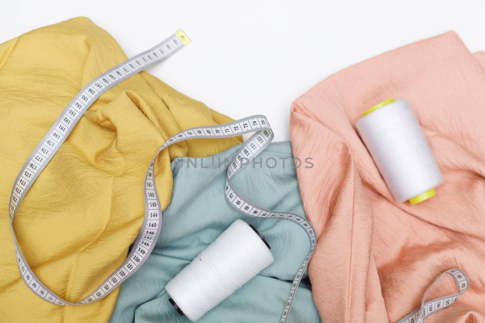 Various fabrics, measuring tape and thread isolated on white. Flat lay
