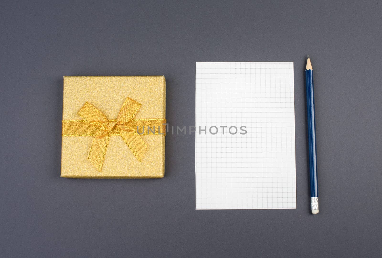 Empty paper, a pen and a golden colored gift on a dark grey background, copy space for text