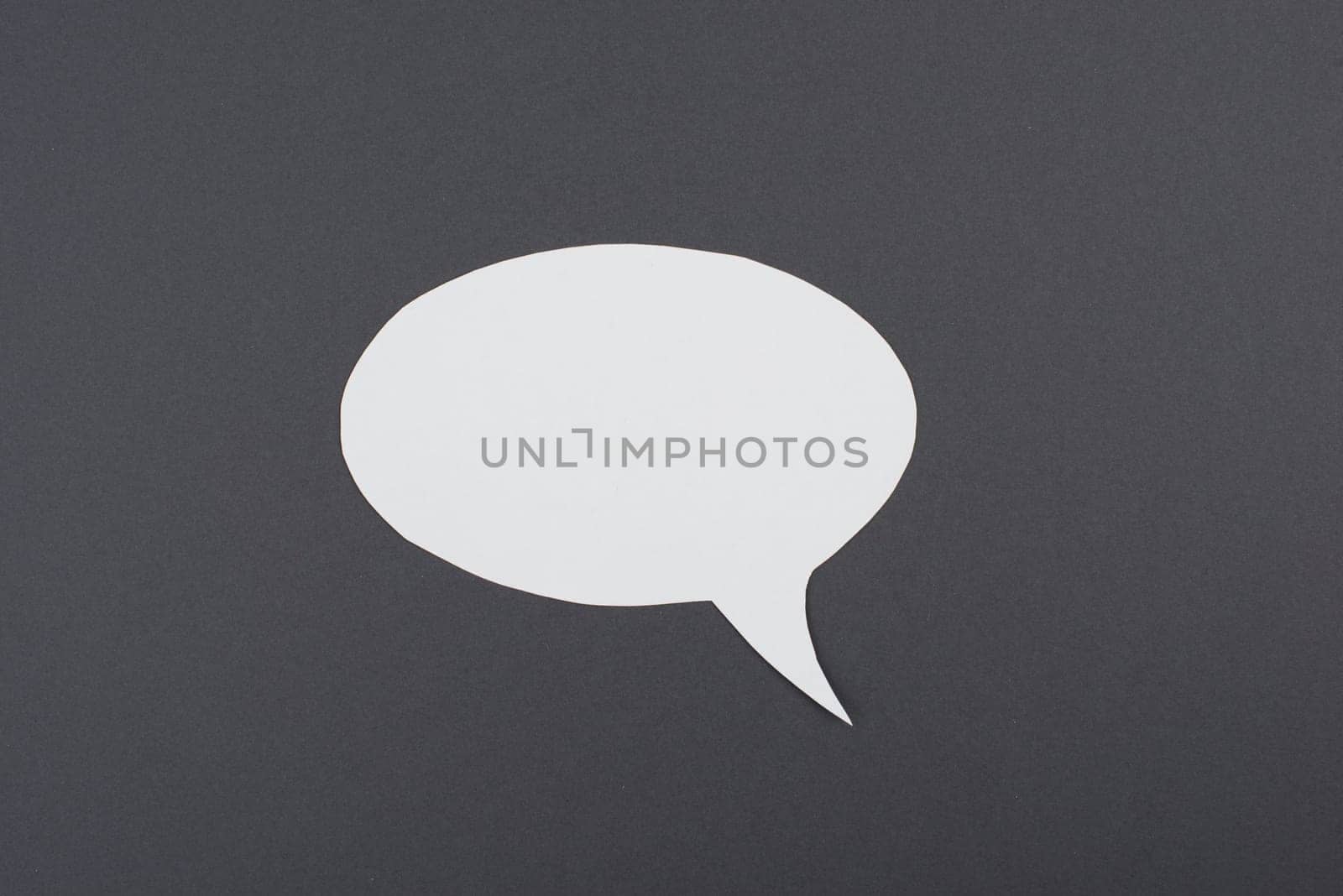 Empty speech bubble, white paper on a dark grey background, copy space for text, communication symbol