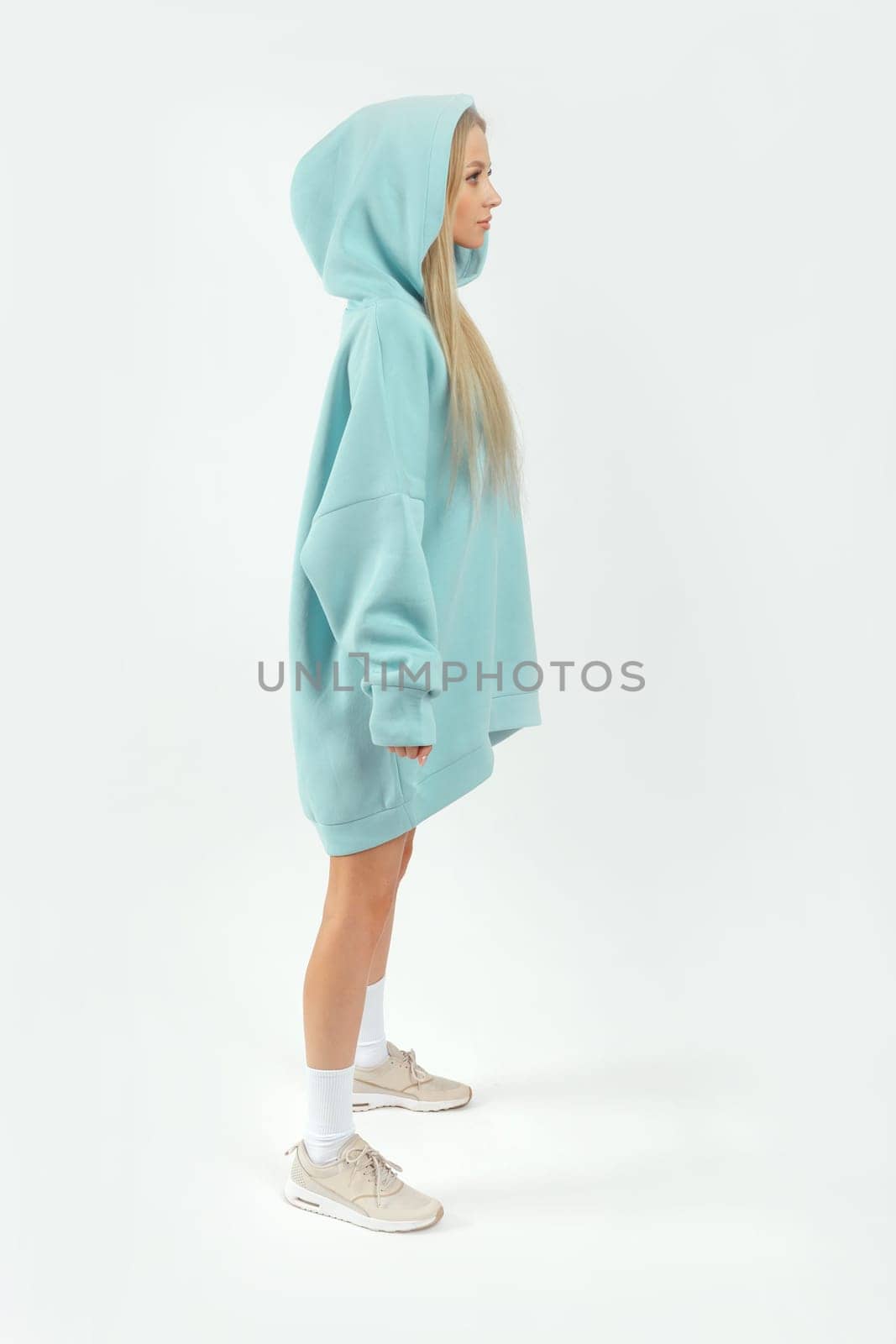 Young pretty woman wearing turquoise hoodie and gray cycling shorts on white background. Casual women sport look