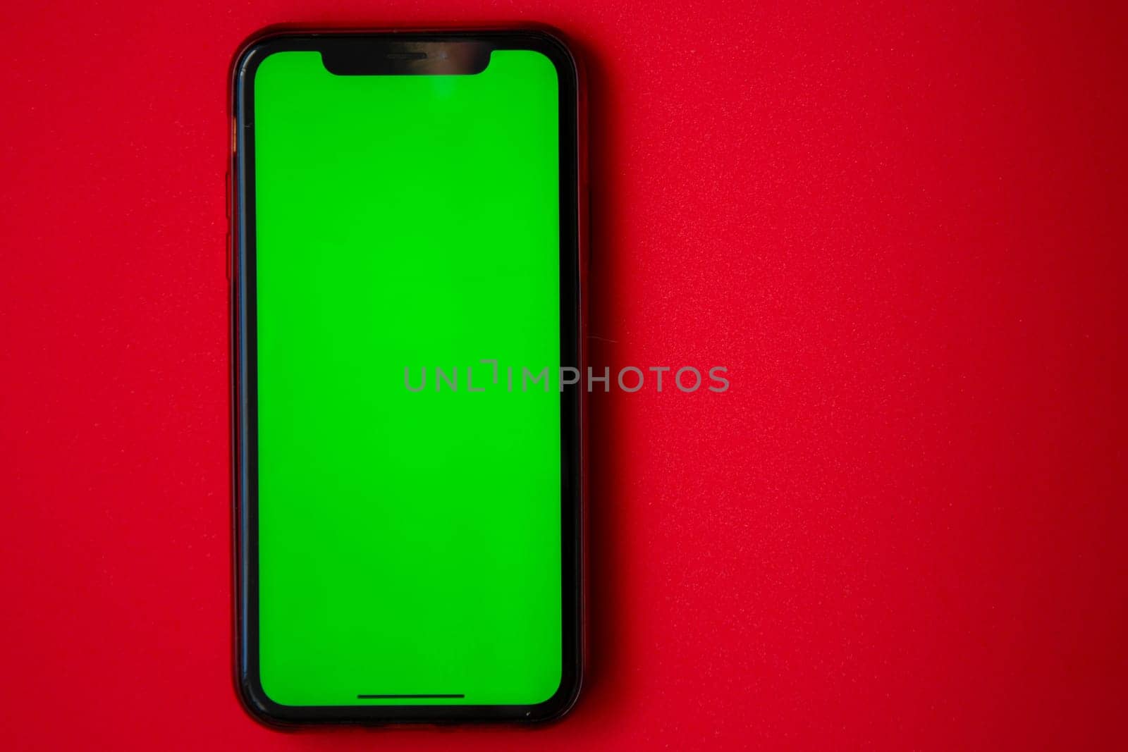 A phone with a green screen is on a red background. High quality photo
