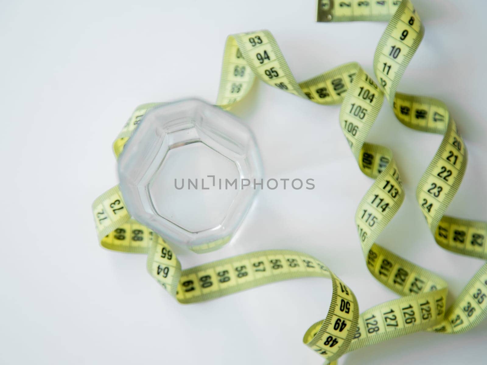 A green apple and a glass of water stand on a white background, they are entwined with a measuring tape. High quality photo