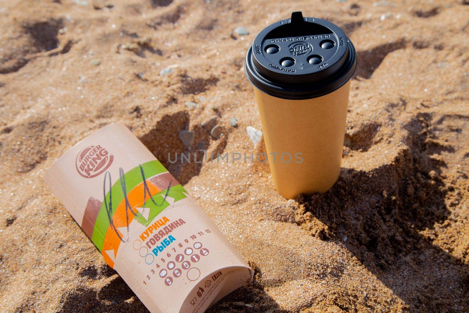Coffee in a disposable cup and burger from Burger King lie on the sand under the sun. High quality photo