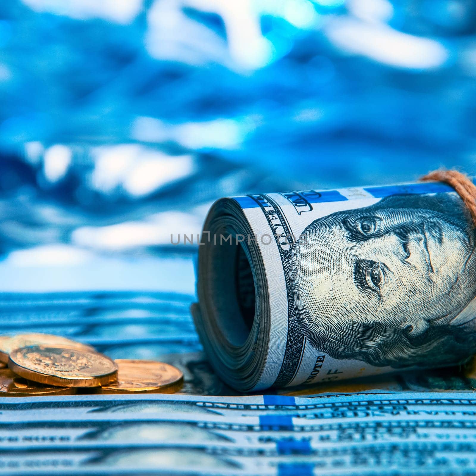 Dollars. A roll of hundred-dollar bills and scattered gold coins lying on the bills on a blue background with a side. Blue style.