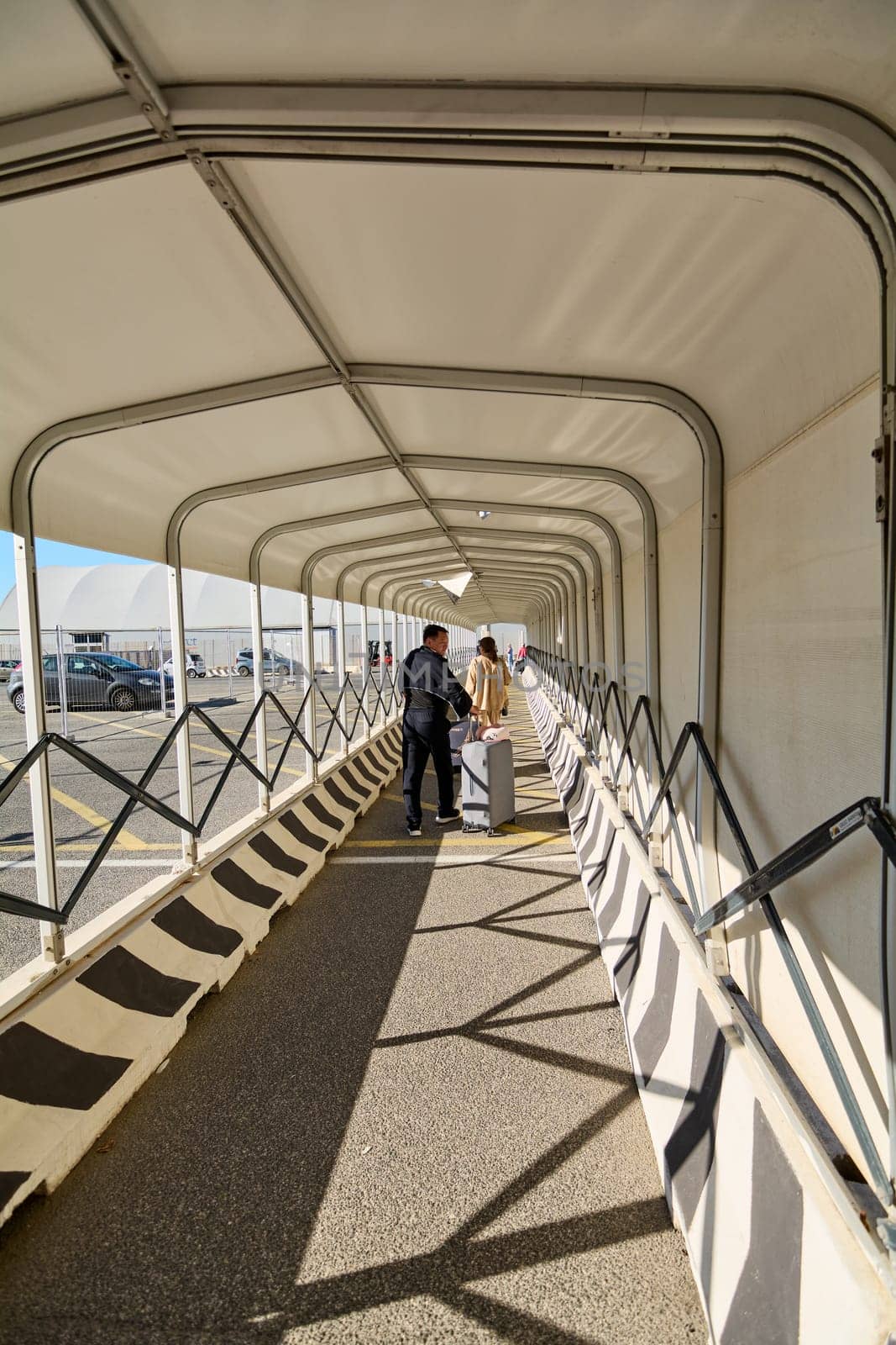 Civitavecchia, Italy - December 19, 2024: Covered walkway at the port with travelers carrying luggage, leading to a parking area. Concept: mobility, tourism, infrastructure.