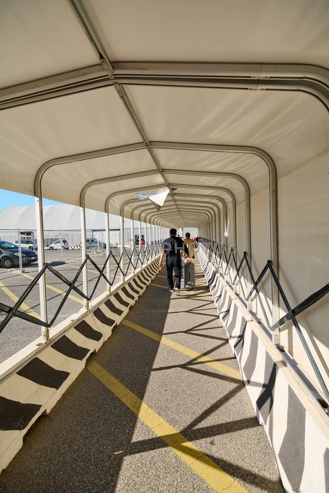 Civitavecchia, Italy - December 19, 2024: Travelers walking through a covered pedestrian passageway with luggage, sunlight filtering through. Concept: transportation, travel, port.