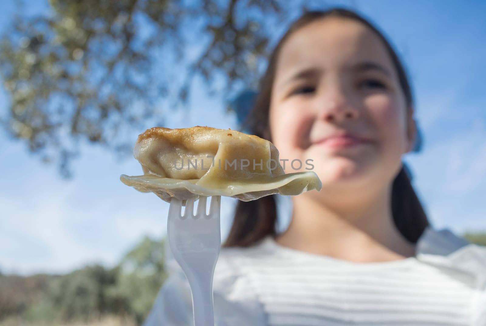 Child girl with jiaozi piece on fork. Outdoors background