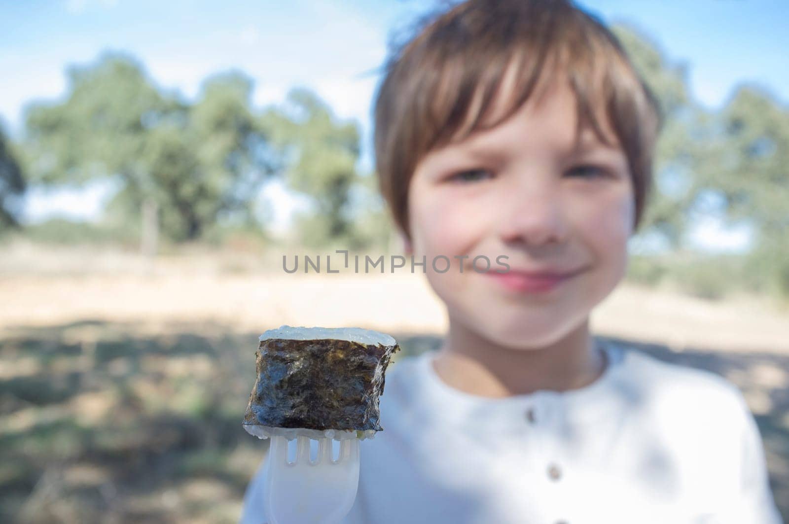 Child boy with sushi maki on fork. Outdoors background