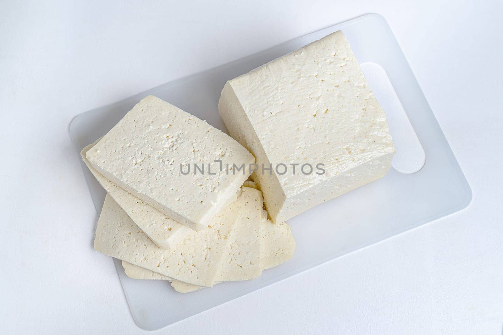 White cheese cut into several pieces on a white surface and white background