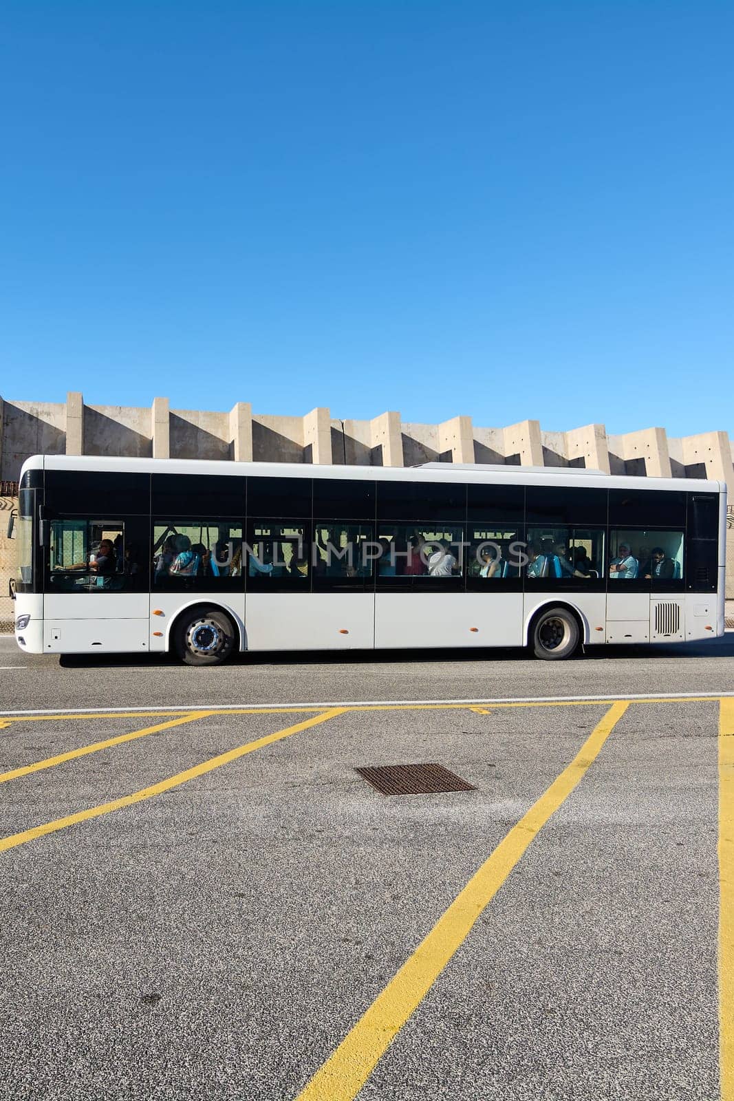 Civitavecchia, Italy - December 19, 2024: A city bus travels along a deserted street, emphasizing public transport in an urban setting The clear sky and concrete barrier offer a modern, clean backdrop