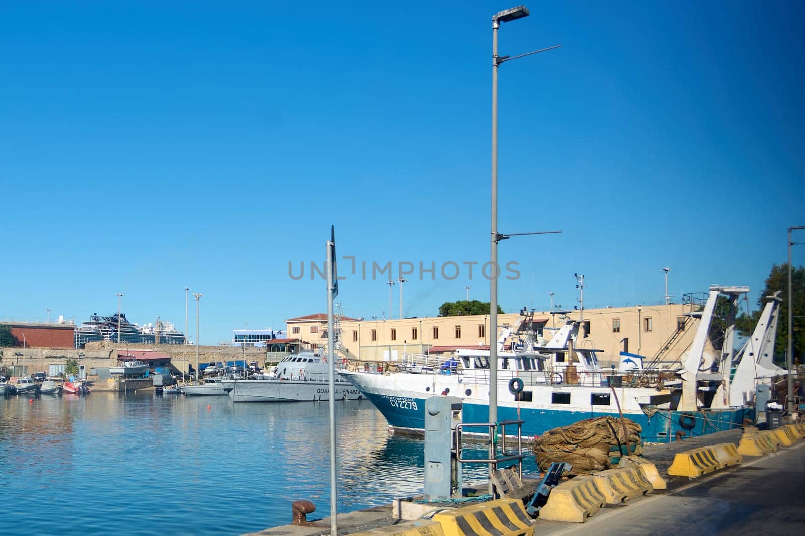 Civitavecchia, Italy - December 19, 2024: Ships, including fishing boats and coast guard vessels, dock in the port of Civitavecchia under a blue sky, highlighting maritime activities and port life.
