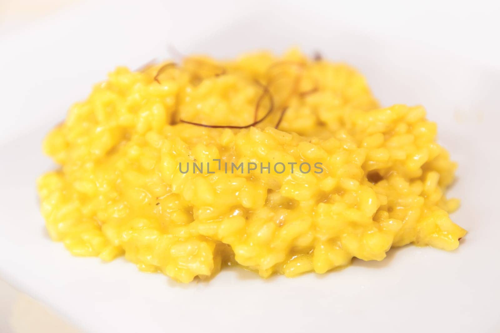 Plate of creamy yellow risotto rice with saffron threads from Milan, Italy. Shallow DOF.