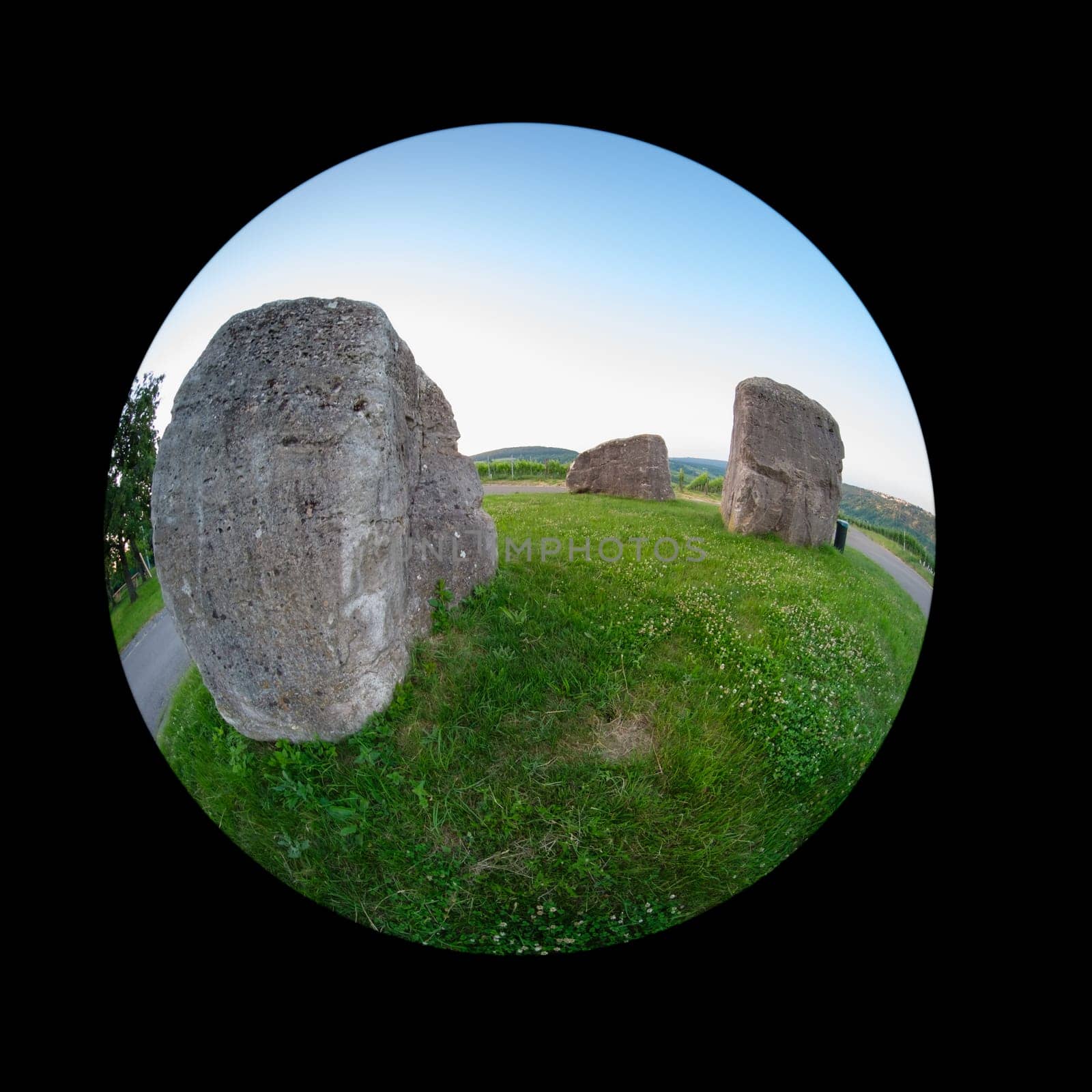 Stone rocke on green meadow with blue sky fish-eye distortion