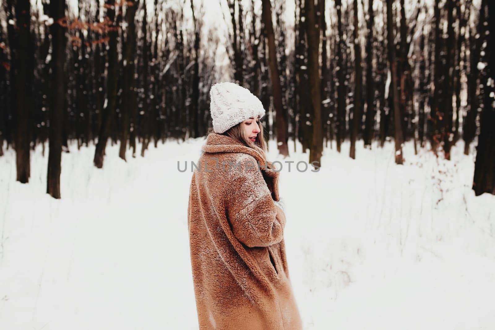 Photo of young beautiful woman in fur coat standing on the white snow in winter forest. Girl is smiling and happy with closed eyes. Female has winter vacation, happily waiting for Christmas holidays