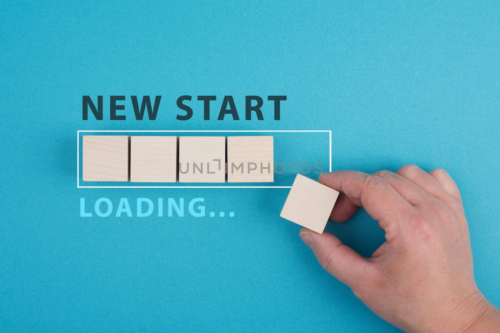 Words new start with a loading bar, hand puts last wooden cube on the blue background, message