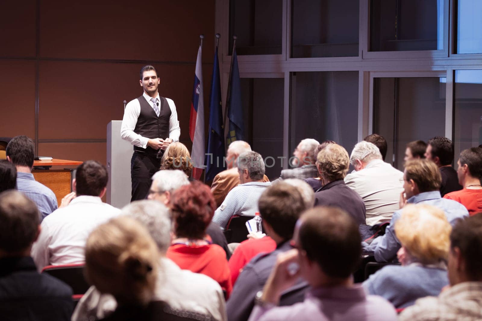 Speaker giving a talk in conference hall at business meeting event. Rear view of unrecognizable people in audience at the conference hall. Business and entrepreneurship concept.