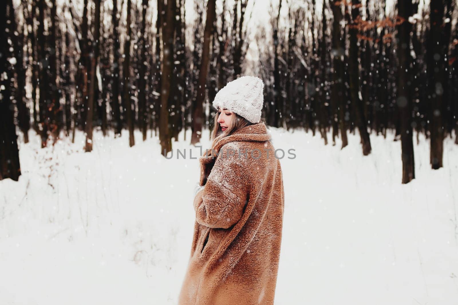 Photo of young beautiful woman in fur coat standing on the white snow in winter forest. Girl is smiling and happy with closed eyes. Female has winter vacation, happily waiting for Christmas holidays