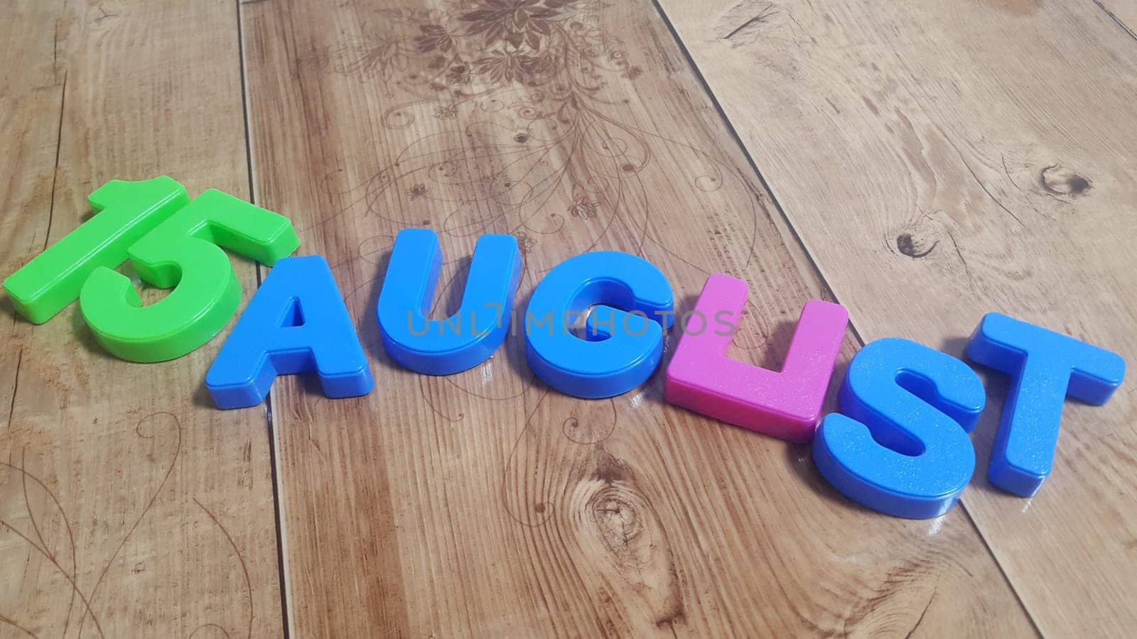 Plastic colored alphabets making words 15 August are placed on a wooden floor. These plastic letters can be used for teaching kids.