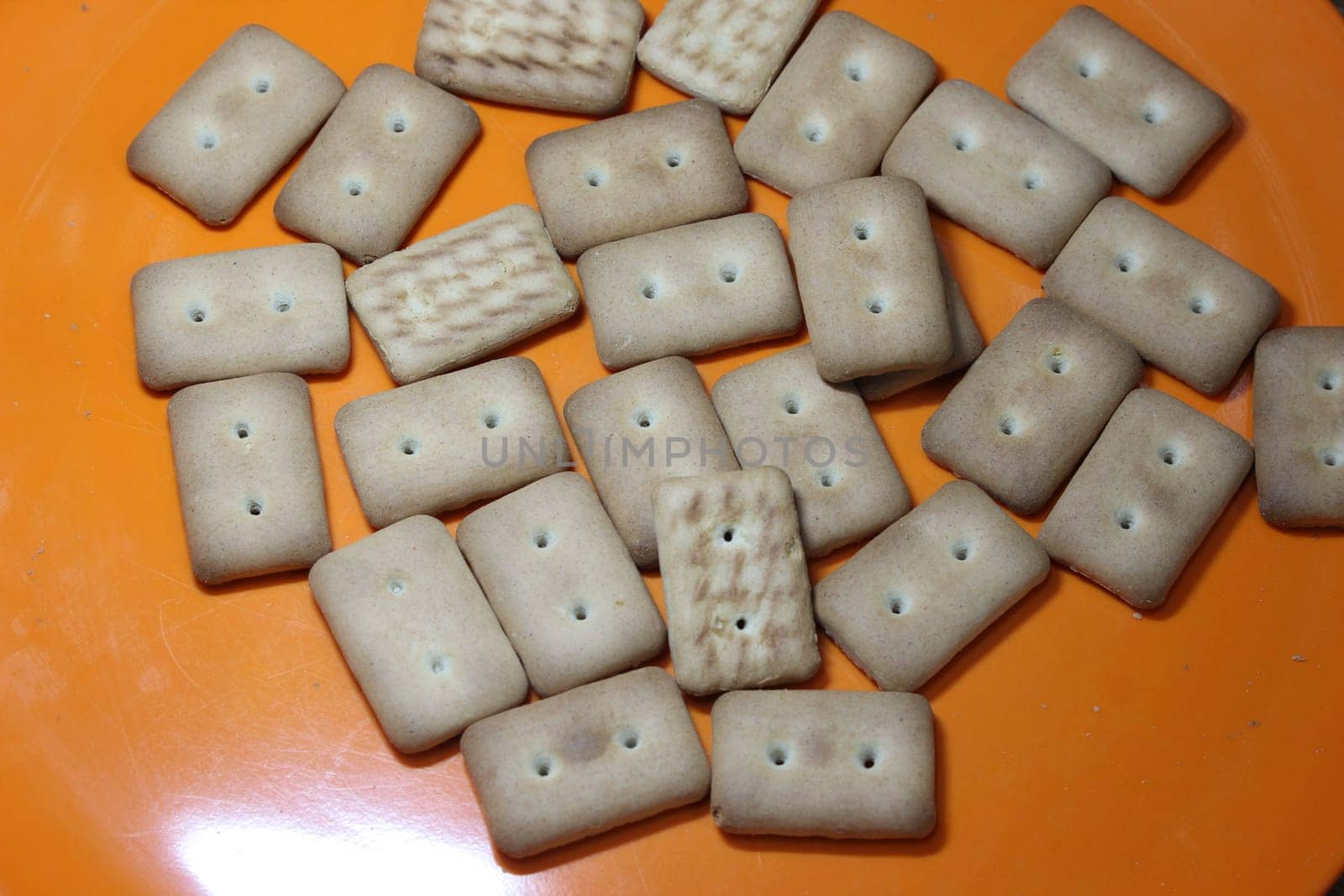 Close up top view of of biscuit cookies. Many rectangular biscuits with small pores in red plate