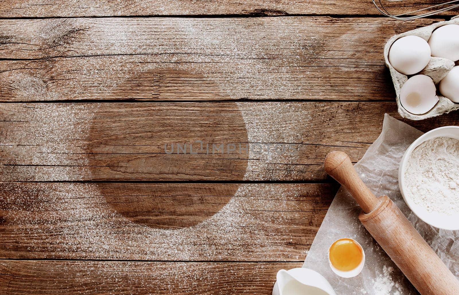Christmas baking ingredients, kitchen utensils on old wooden background. Cooking dough, preparing egg yolk, flour, rolling pin, parchment paper, whisk, salt. Concept flat lay photo with copy space