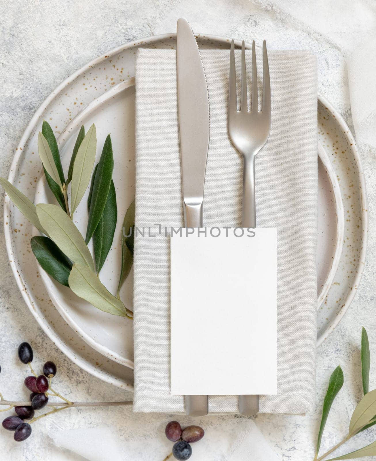 Wedding Table place with place card and porcelain plates decorated with olive branches top view. Elegant modern template with vertical blank paper card flat lay. Mediterranean mockup, copy space