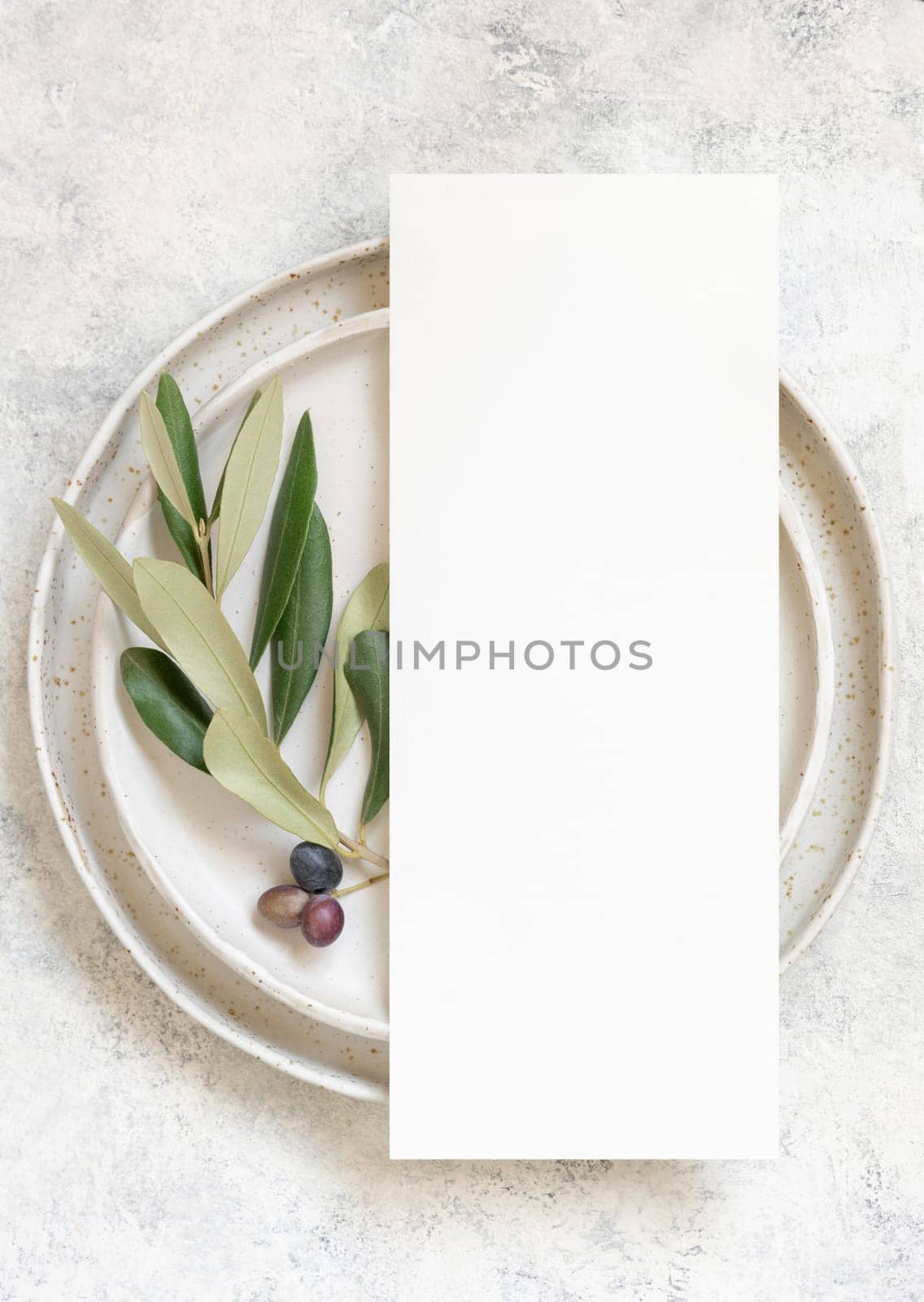 Wedding Table place with a menu card and porcelain plates decorated with olive branches top view. Elegant modern template with vertical blank paper card flat lay. Mediterranean mockup, copy space