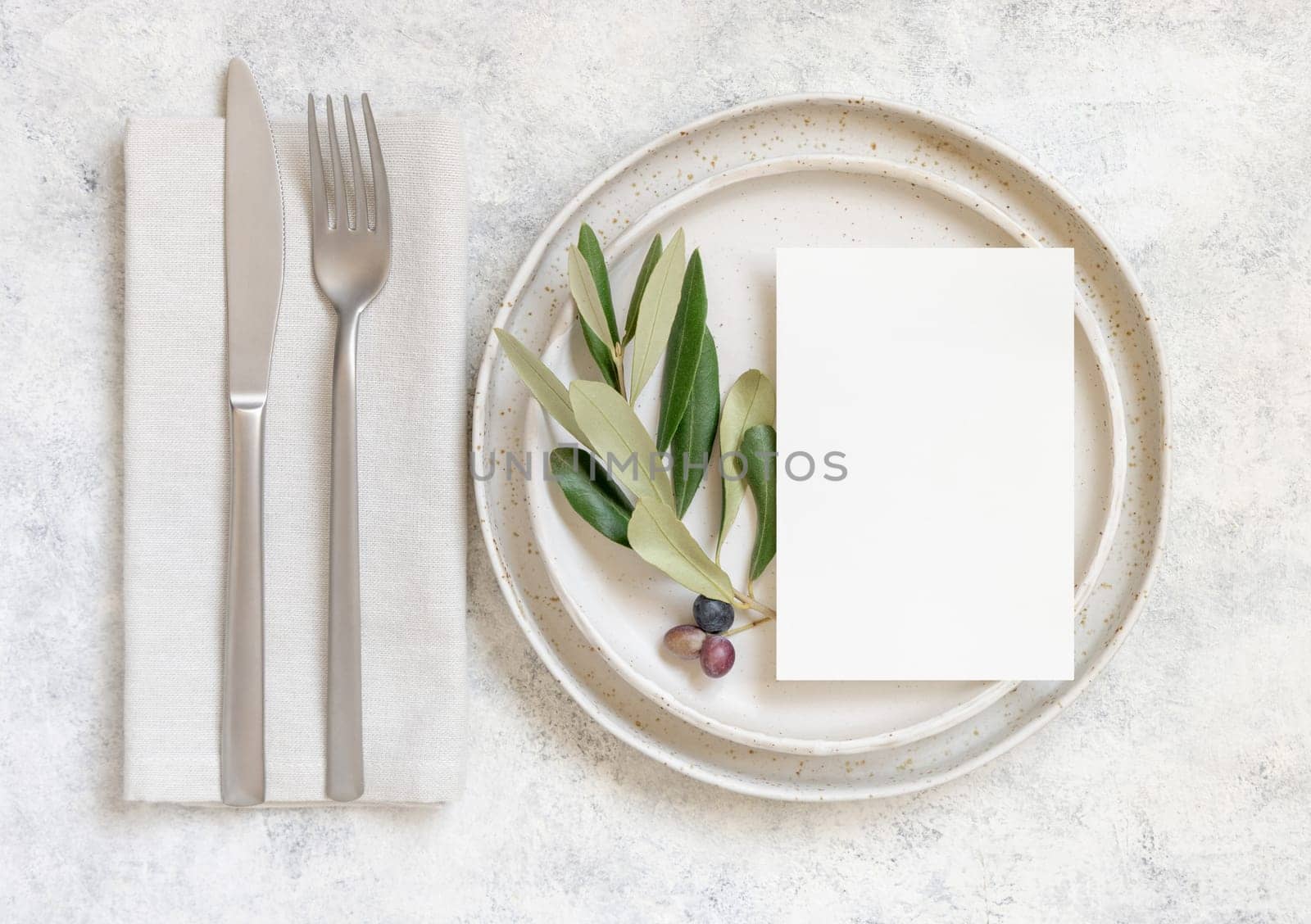 Wedding Table place with invitation card and porcelain plates decorated with olive branches top view. Elegant modern template with vertical blank paper card flat lay. Mediterranean mockup, copy space