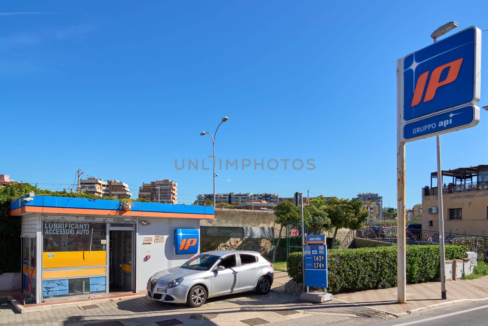 Civitavecchia, Italia - December 27, 2024: A fuel station with a modern car and clear signage, framed by an urban skyline under a bright blue sky. Concept: City life and transportation essentials.