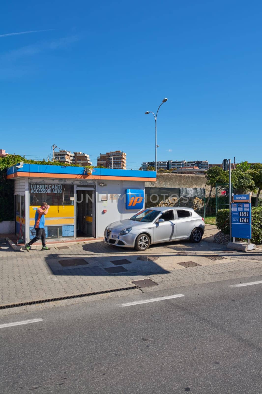 Civitavecchia. Italia  - December 27, 2024:  Urban gas station in Civitavecchia, Italy, with a parked car. Modern IP station with blue sky and urban buildings, showing the concept of urban refueling.