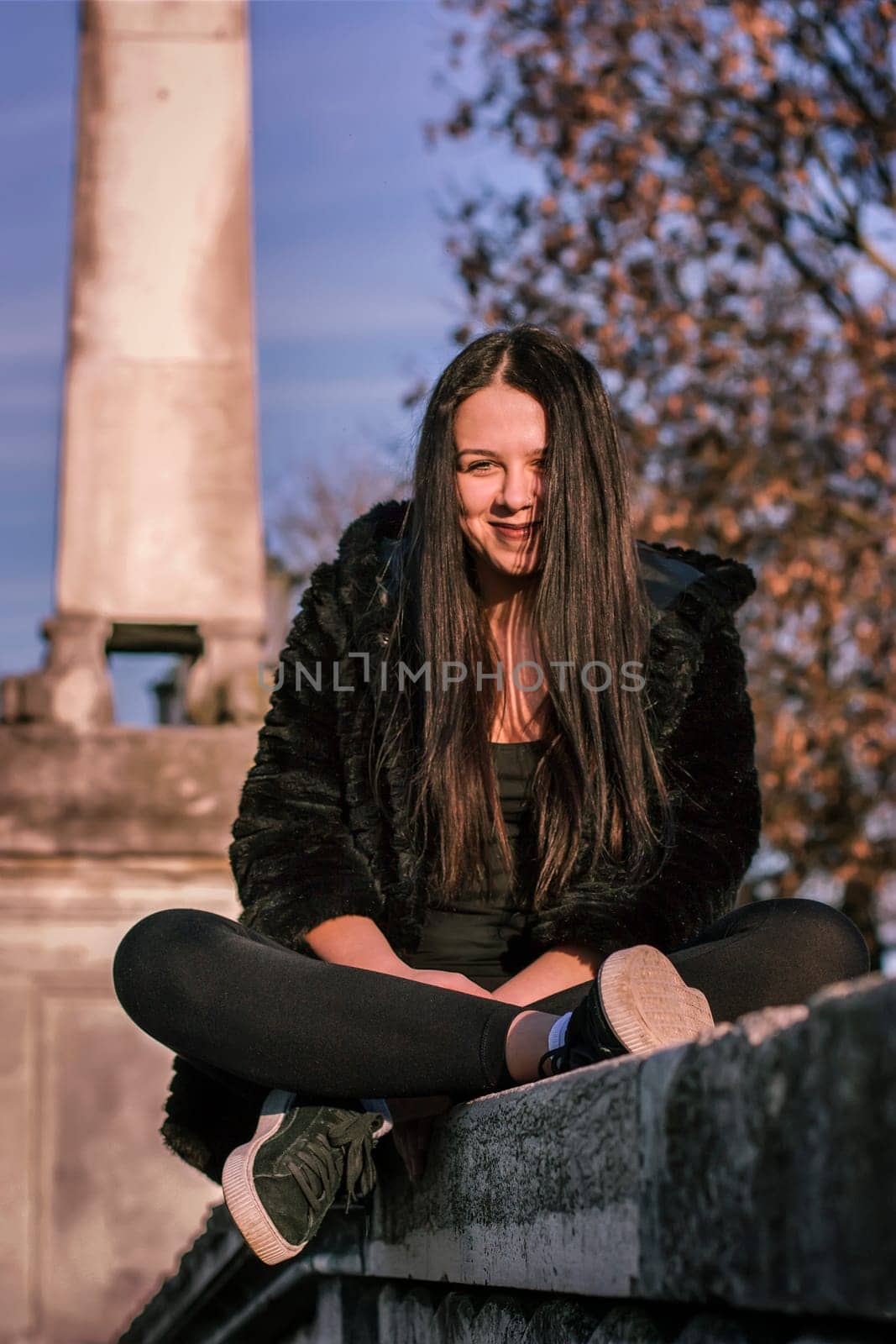 Portrait of Smiling teen girl sitting on the low wall with her legs crossed