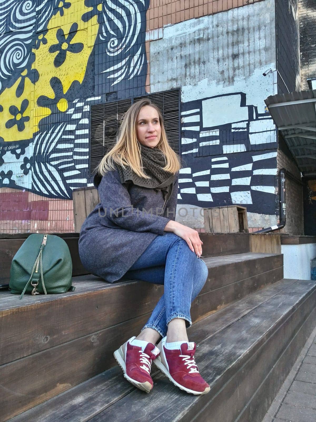 A young woman sits on a wooden staircase near a building in a bohemian quarter in the autumn